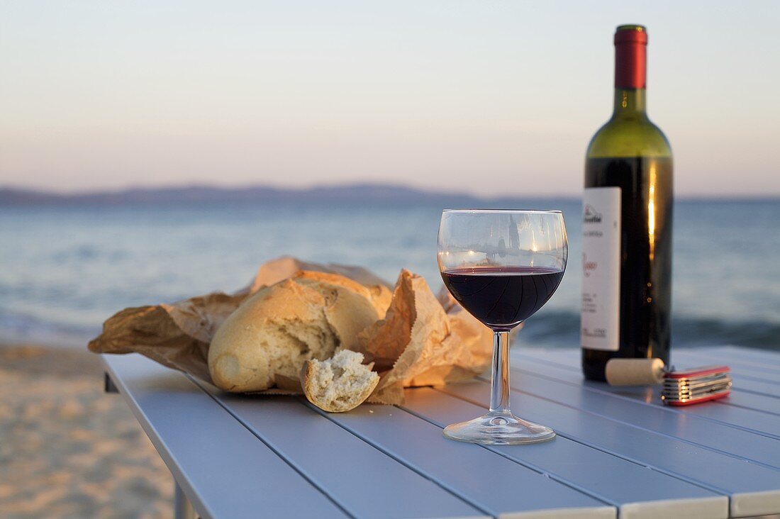 Rotweinglas, Rotweinflasche und Brot auf Tisch am Meer