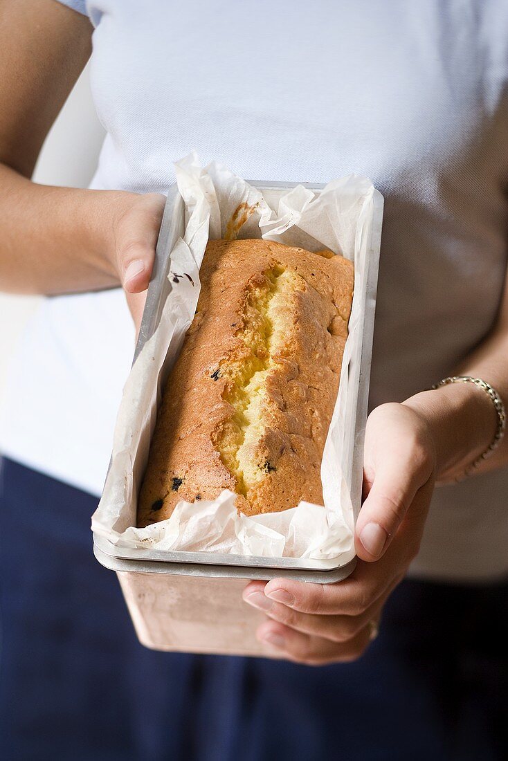 Woman holding plum loaf in loaf tin