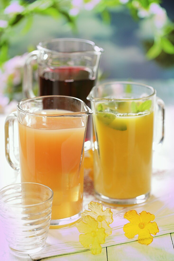 Three different fruit juices in glass jugs