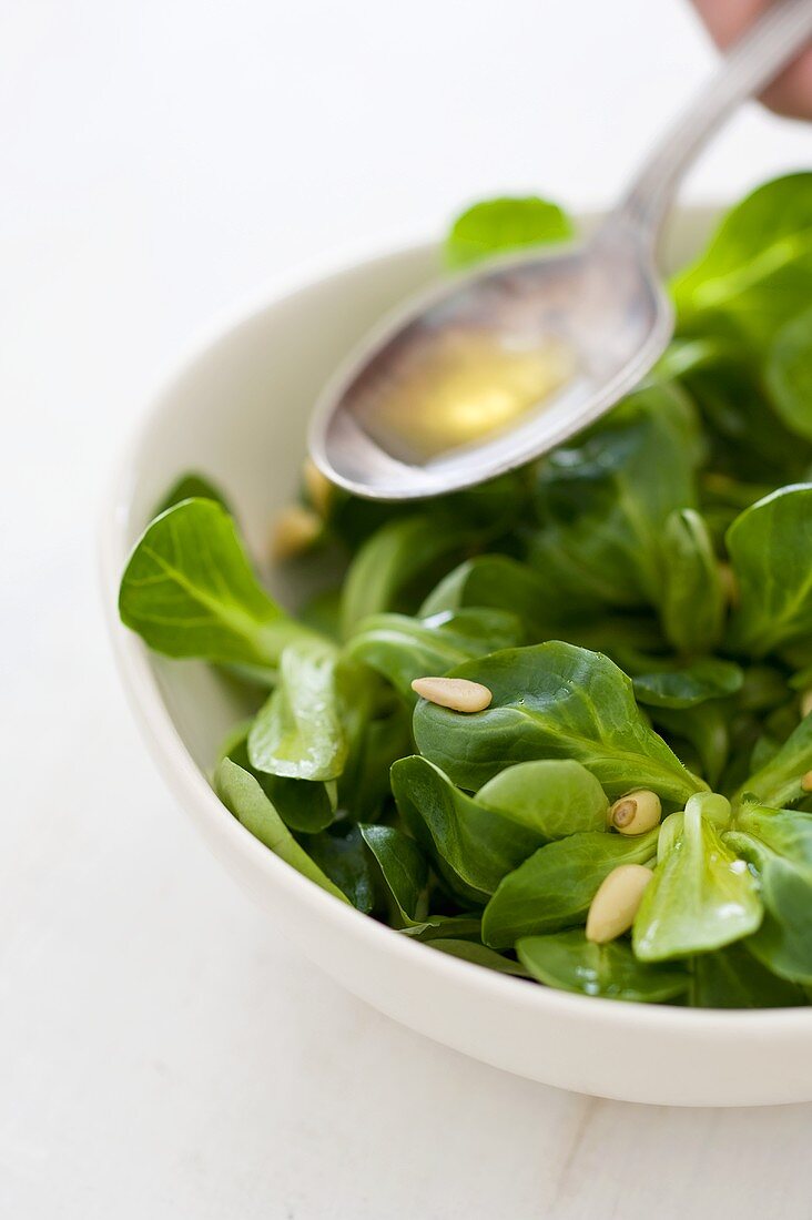 Feldsalat mit Pinienkernen mit Öl beträufeln