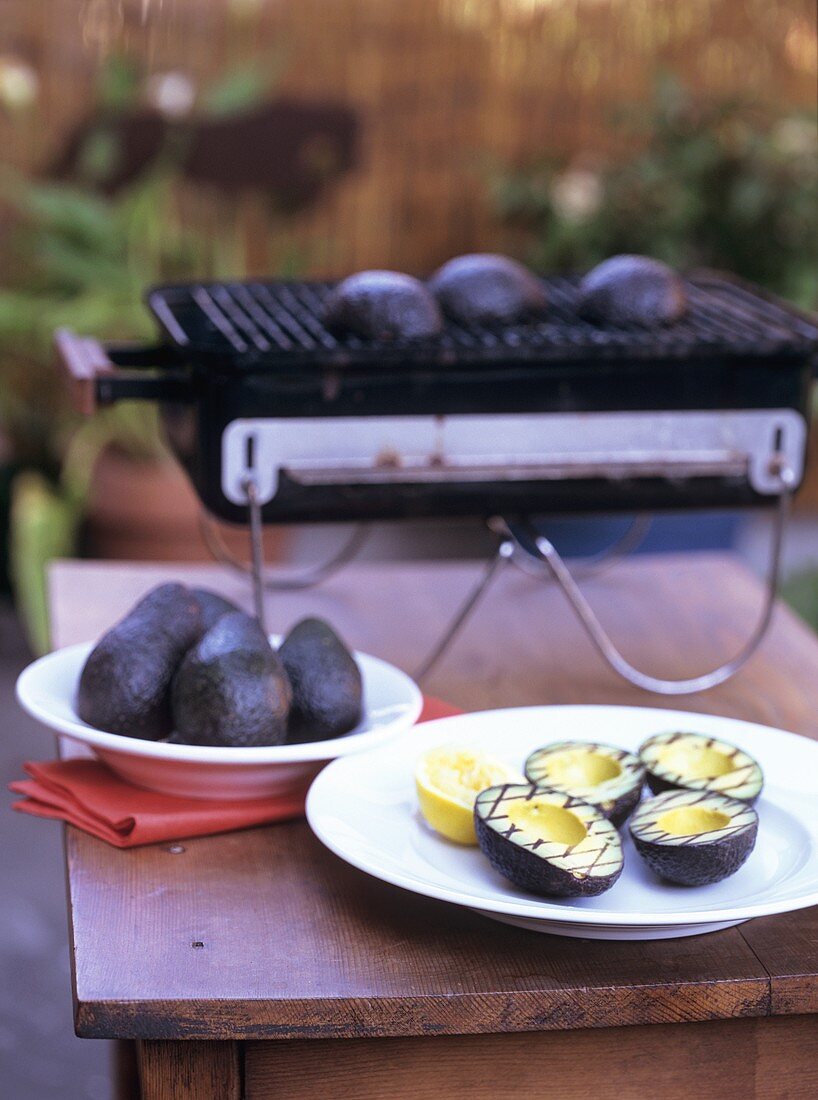 Gegrillte Avocadohälften auf einem Teller und auf dem Grill