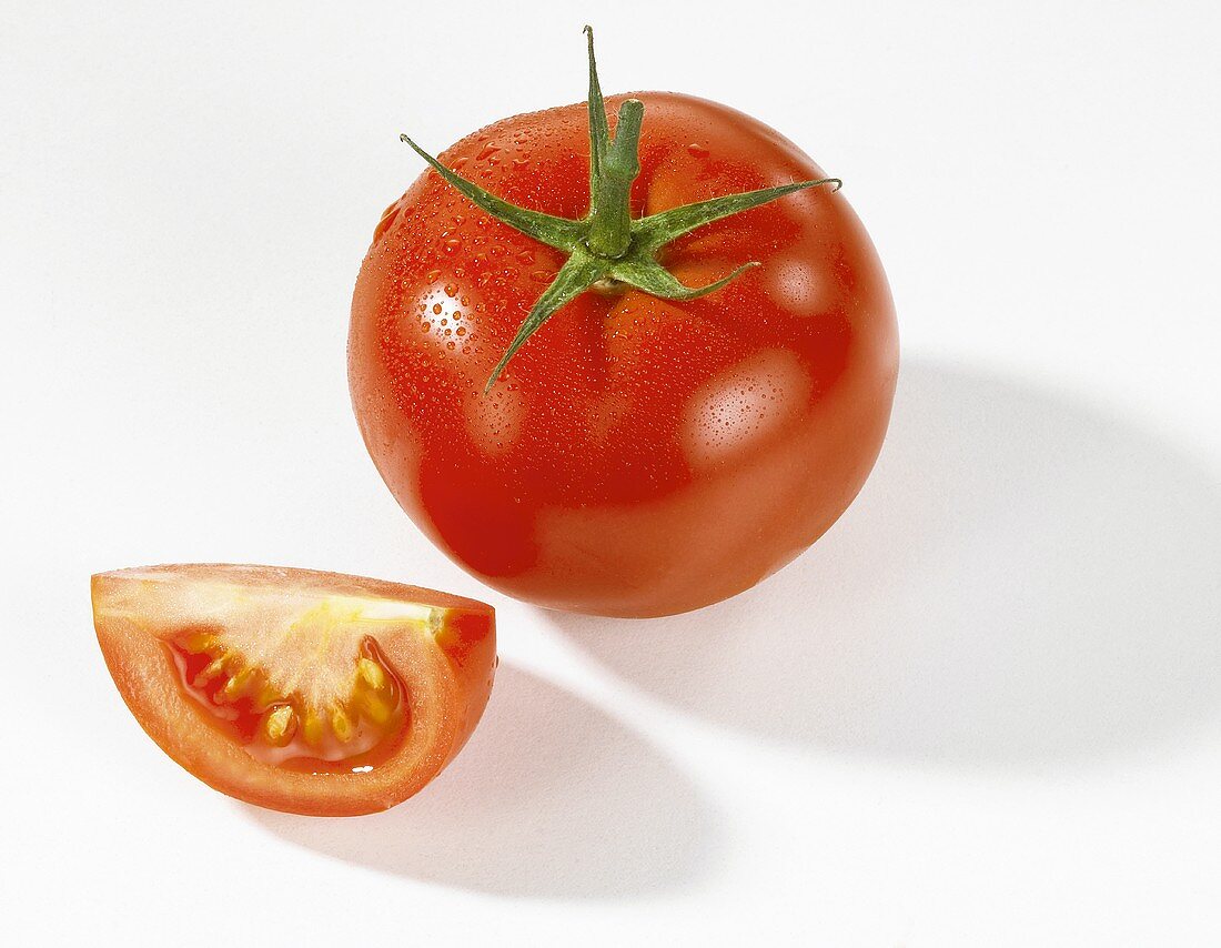 Whole tomato and wedge of tomato with drops of water