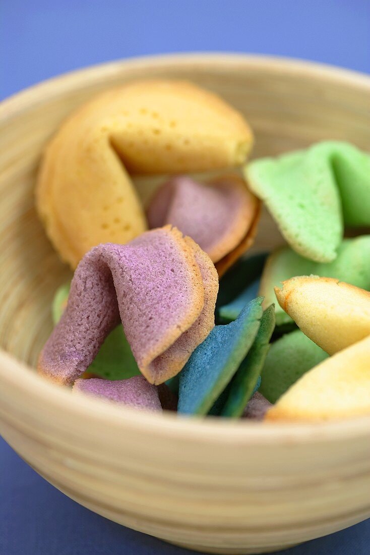 Different-coloured fortune cookies in wooden bowl
