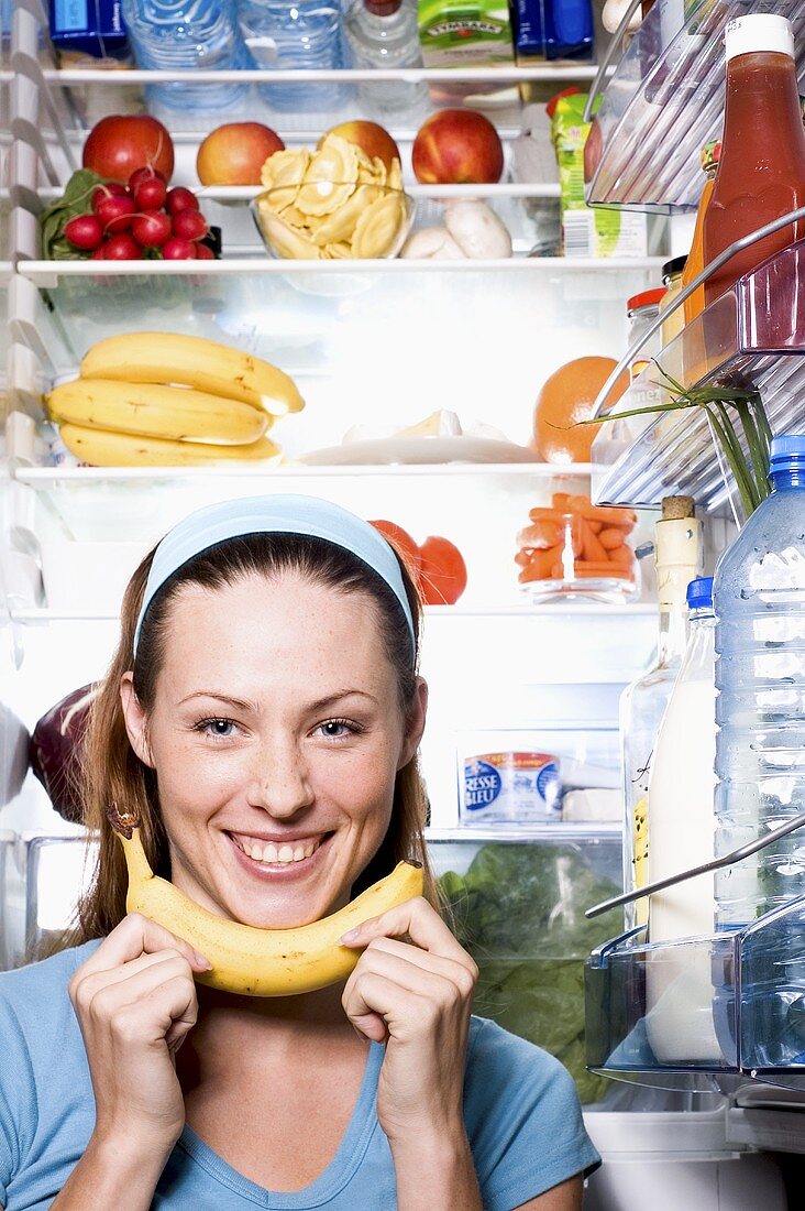 Junge Frau mit Banane vor geöffnetem Kühlschrank