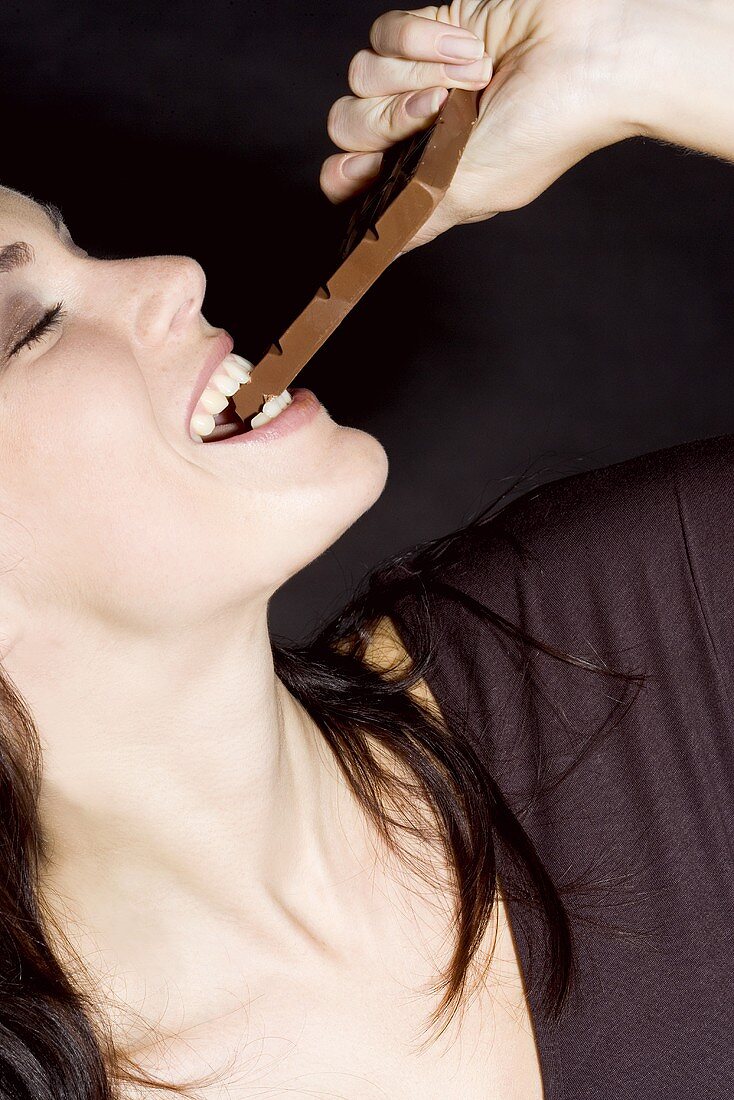 Junge Frau beisst in eine Schokoladentafel