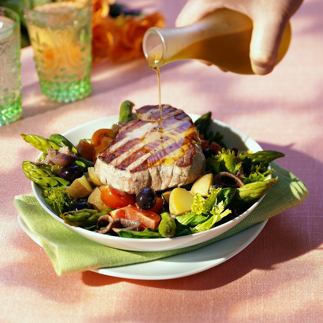Pouring olive oil over tuna steak on vegetable salad