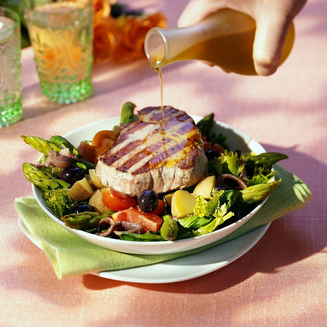 Thunfischsteak auf Gemüsesalat wird mit Olivenöl begossen