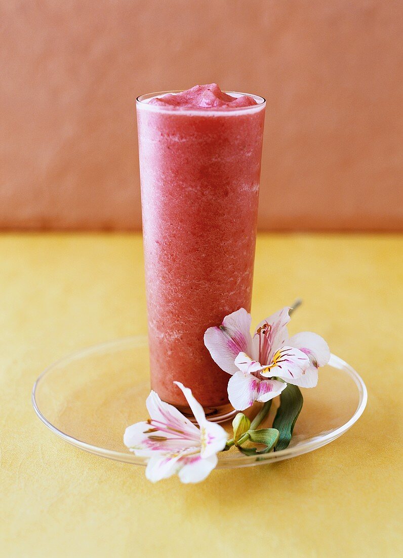 Erdbeer-Vanille-Drink neben Blüten auf einem Glasteller