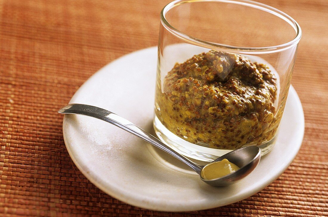 Small spoonful of mustard, glass of whole-grain mustard behind