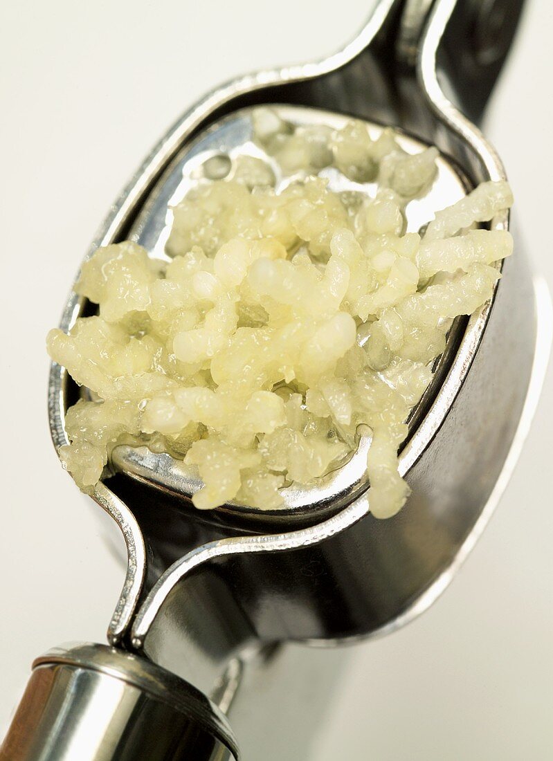 Garlic being pressed through a garlic press