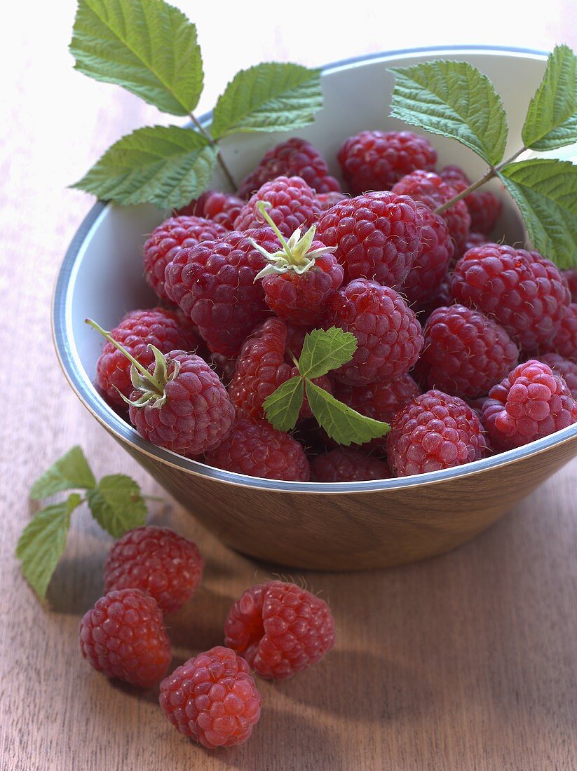 Raspberries in and in front of a small bowl
