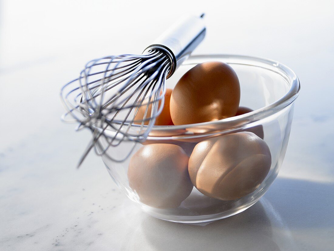 Brown eggs in a glass bowl, whisk on bowl