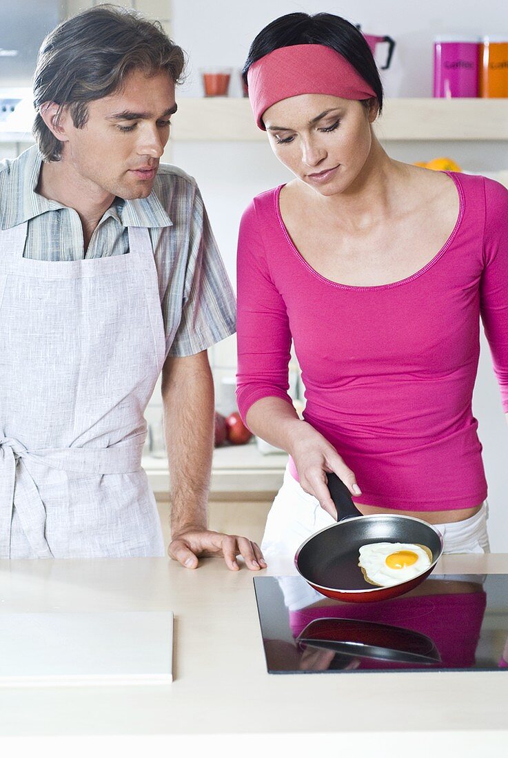 Man and woman frying an egg on hob