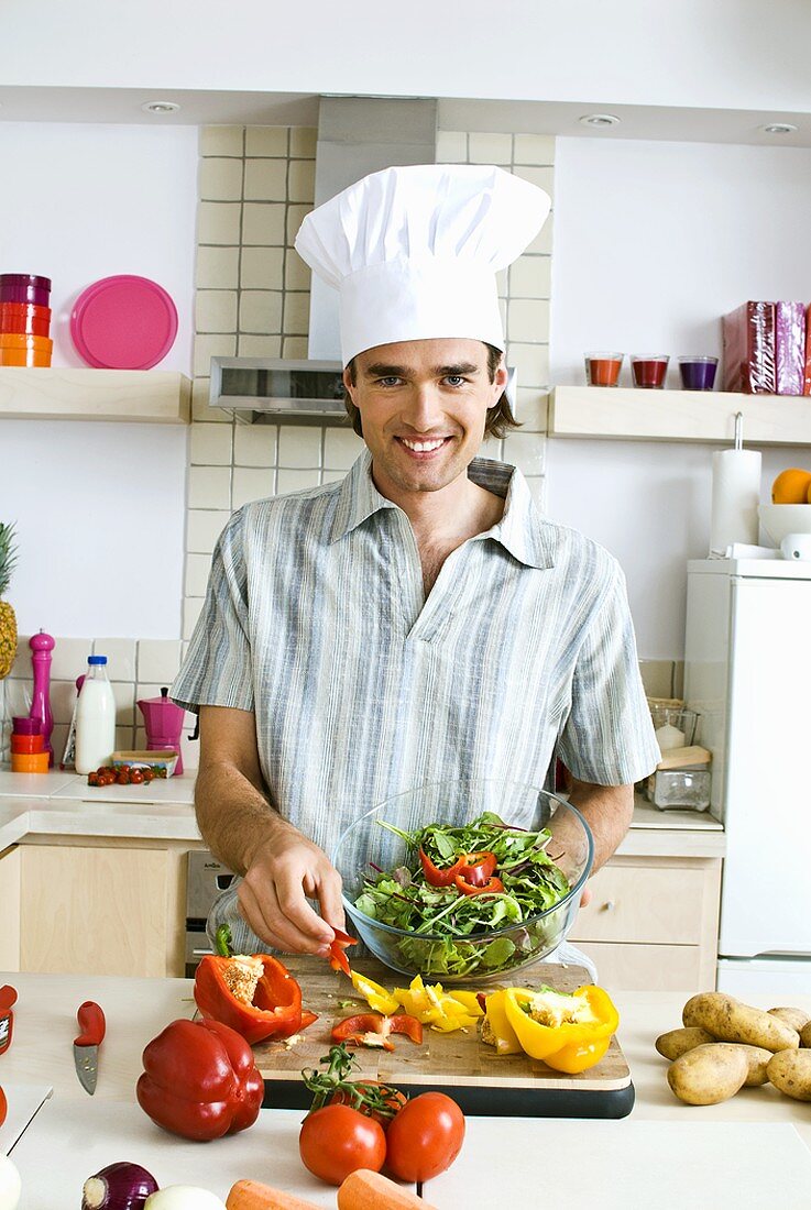 Mann mit Kochmütze bereitet Salat zu