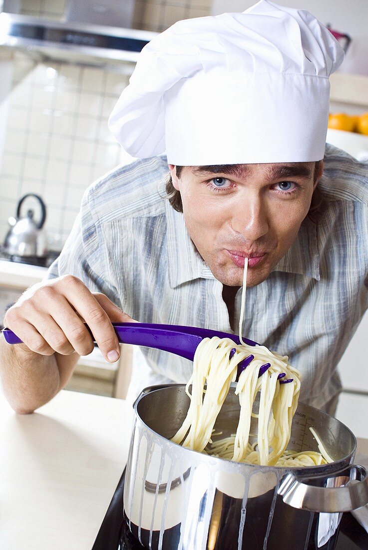 Man in chef's hat eating pasta out of pan