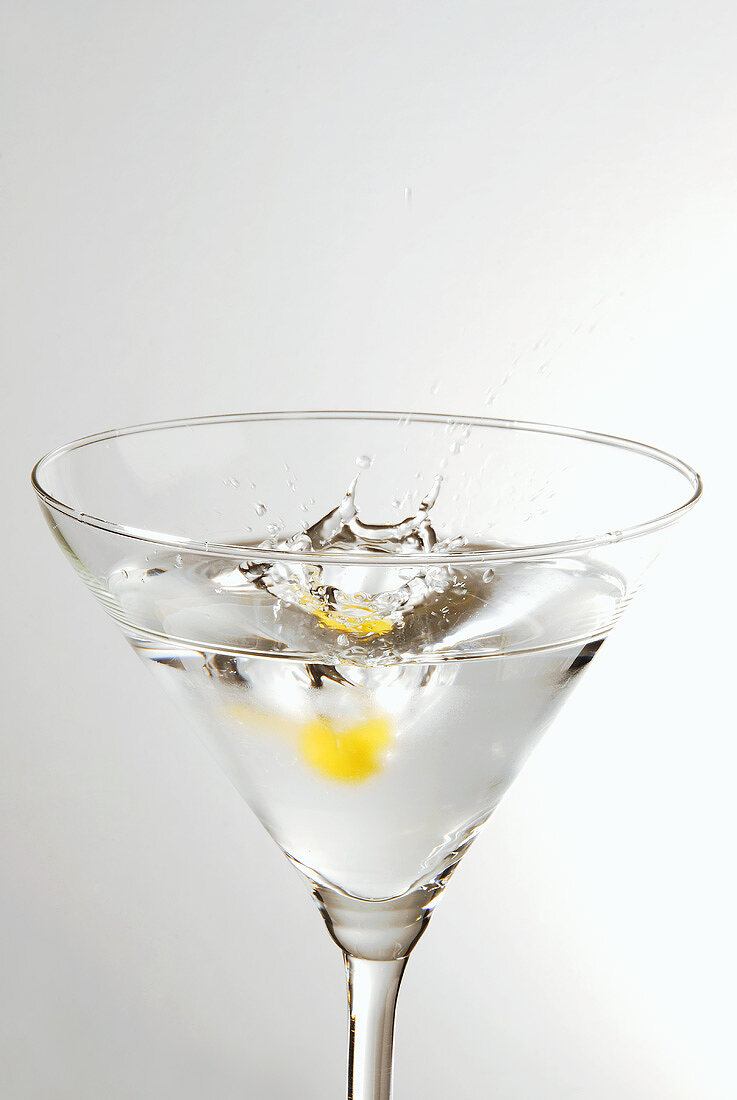 Stück Zitronenschale fällt in ein Glas Martini