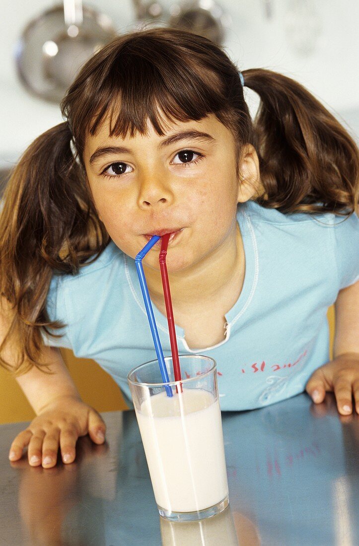 Kleines Mädchen trinkt ein Glas Milch mit zwei Strohhalmen