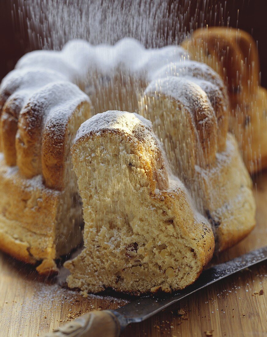 Icing sugar falling onto yeast gugelhupf with raisins