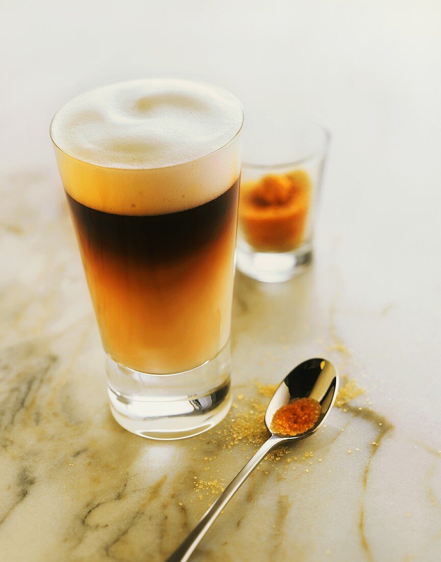 Glas Latte Macchiato und ein Löffel mit braunem Zucker