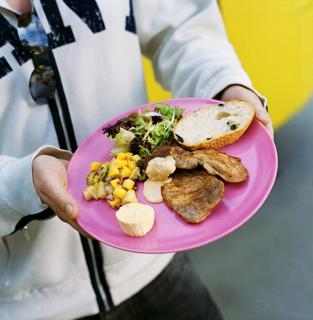 Man holding plate of grilled meat and salads