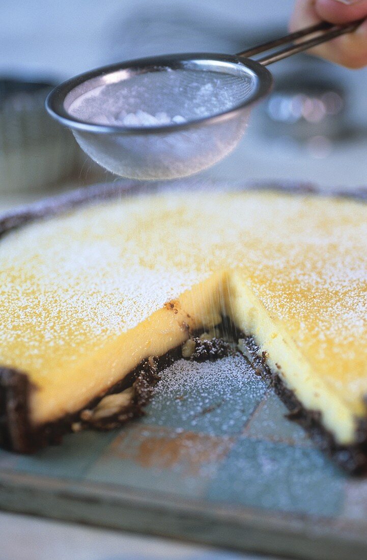 Sieving icing sugar over lemon tart with chocolate crust