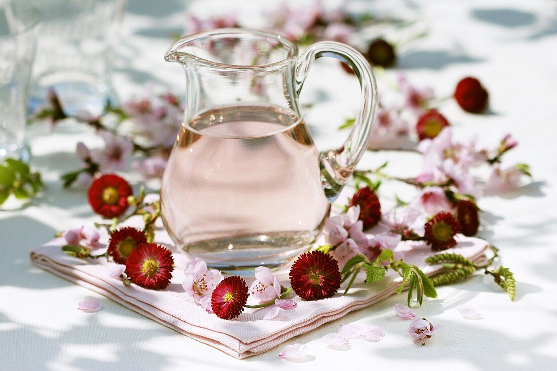 Rose syrup in jug surrounded by Bellis and peach blossom