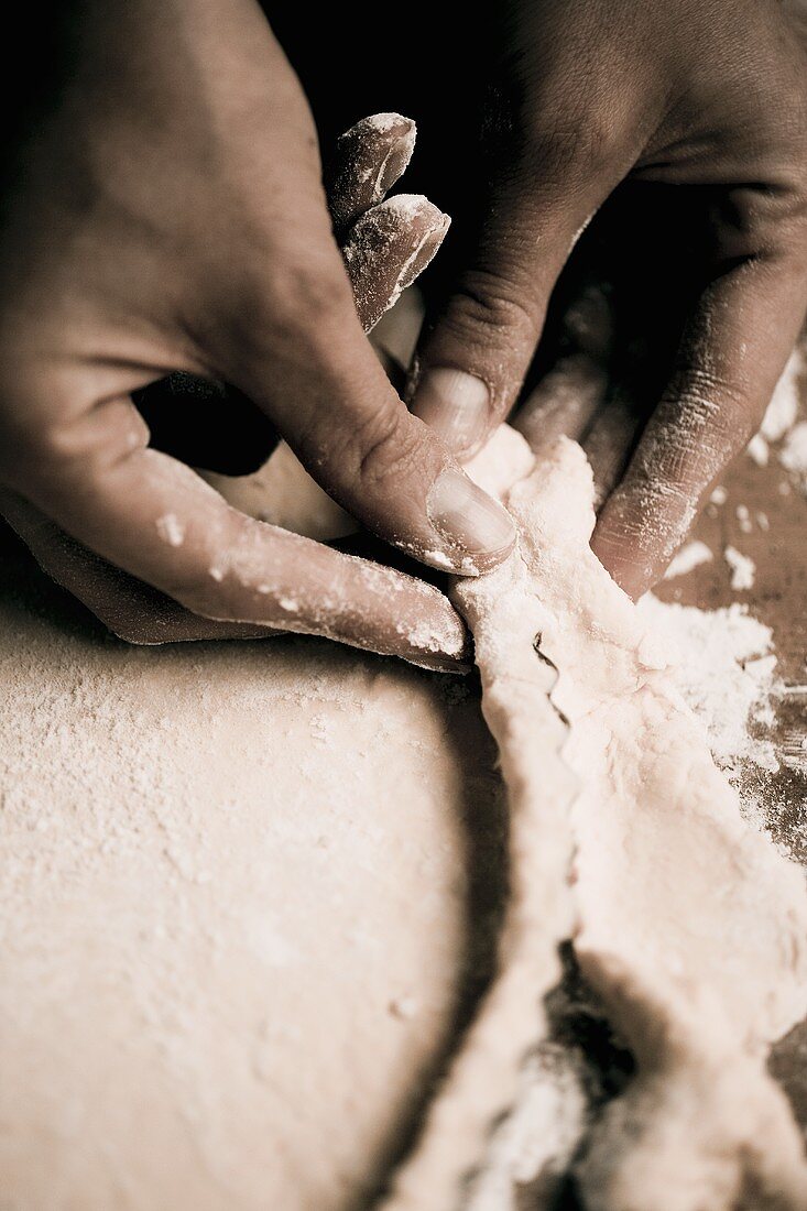 Hands pressing pastry onto the sides of a tart tin