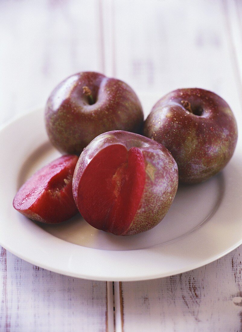 Two whole plums & one with a piece cut off on a plate
