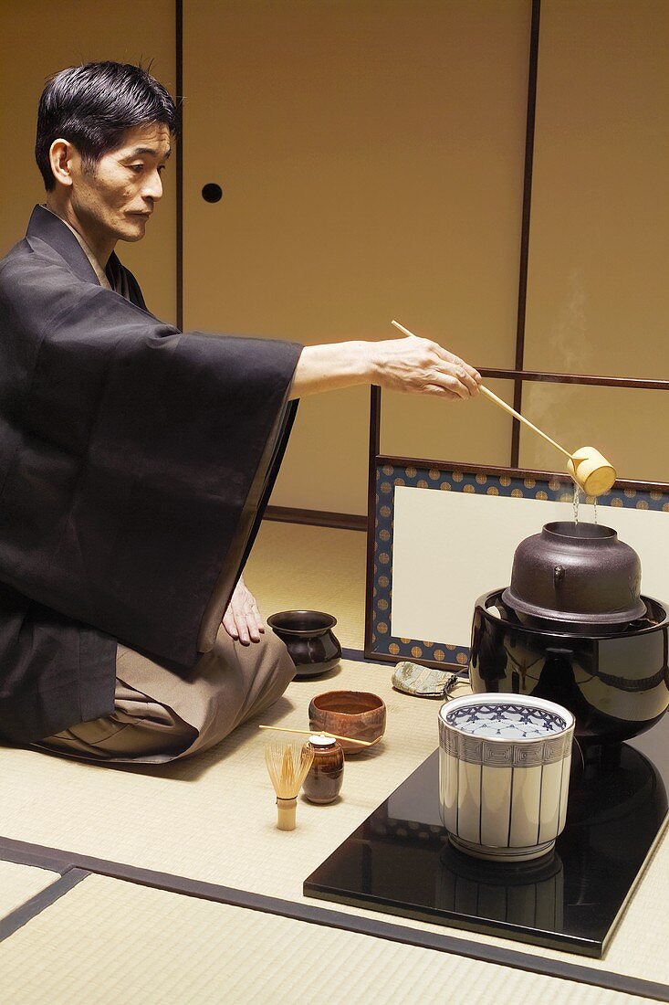 Tea master at tea ceremony, pouring water into kettle