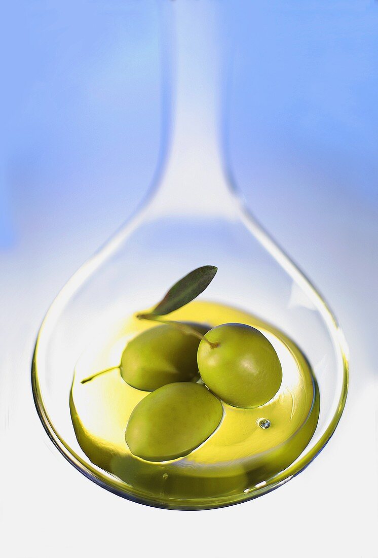 Ein Löffel mit Olivenöl und drei Oliven