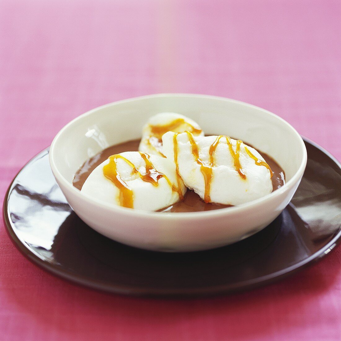 Poached meringues with caramel sauce on chocolate pudding