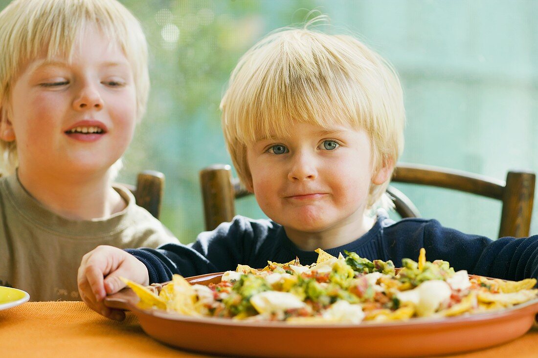 Two boys, nachos with tomato salsa and guacamole