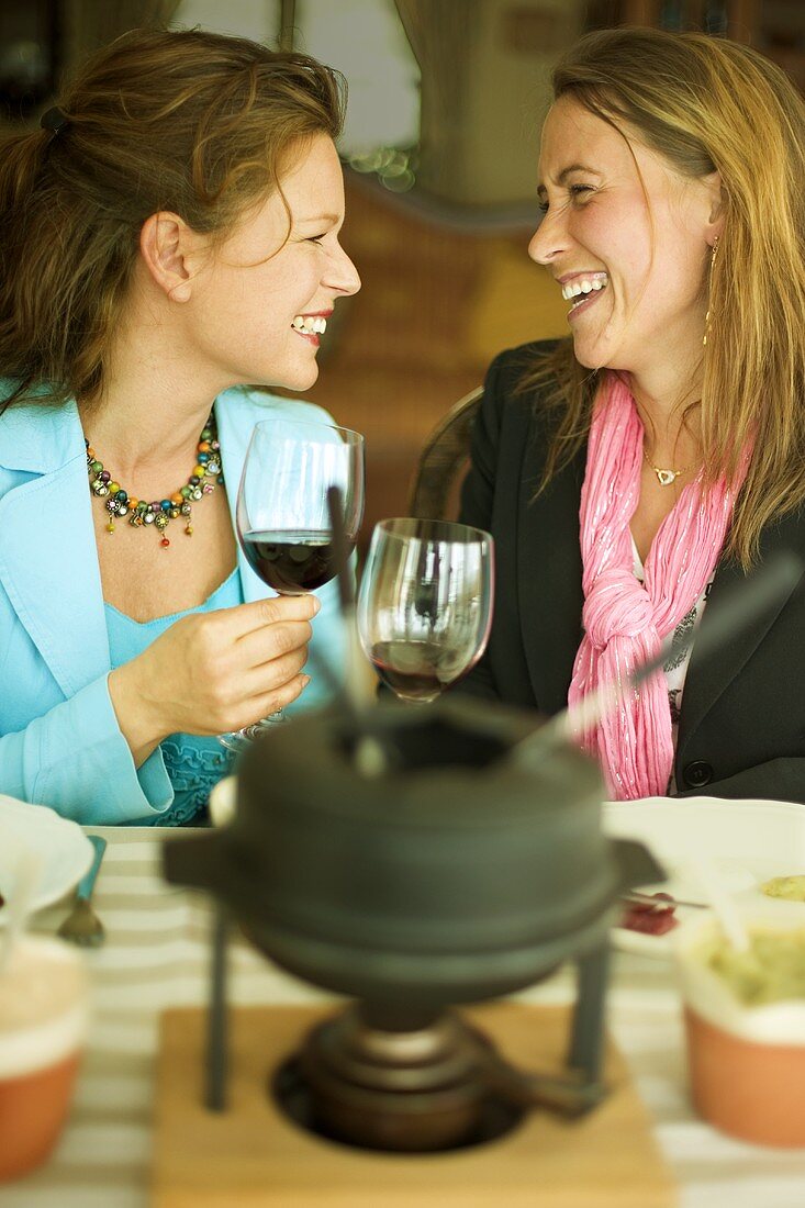 Zwei Frauen stossen beim Fondue essen mit Wein an