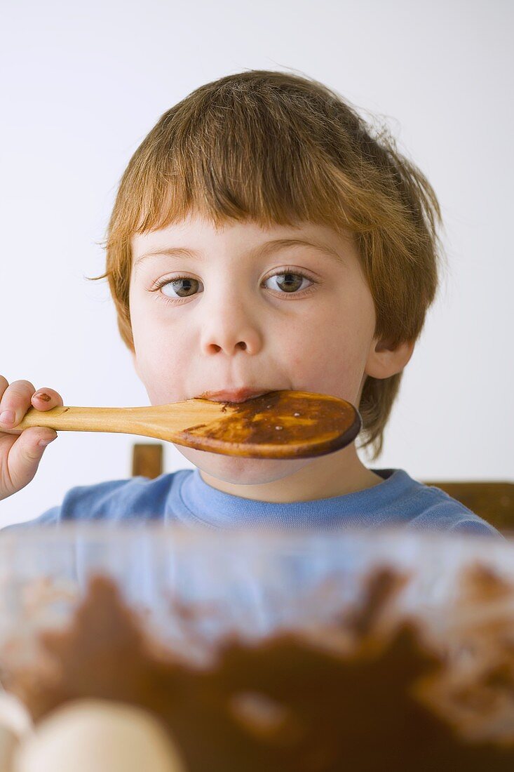 Small boy licking a wooden spoon