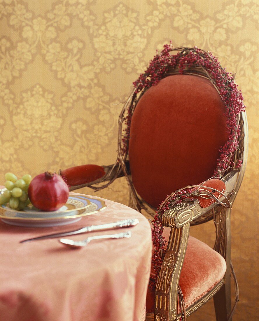 Table with pomegranate and grapes on plate, chair