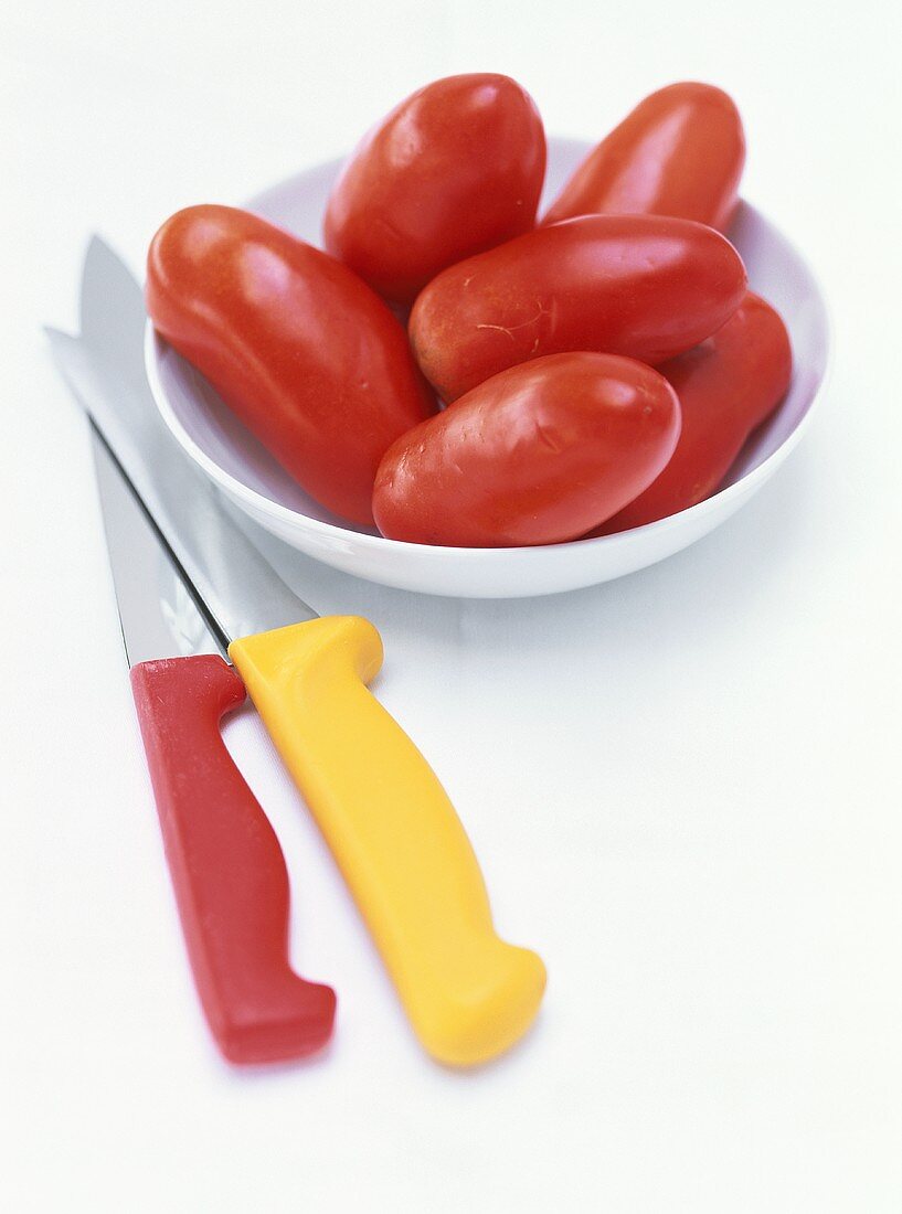 Plum tomatoes in a dish, two kitchen knives