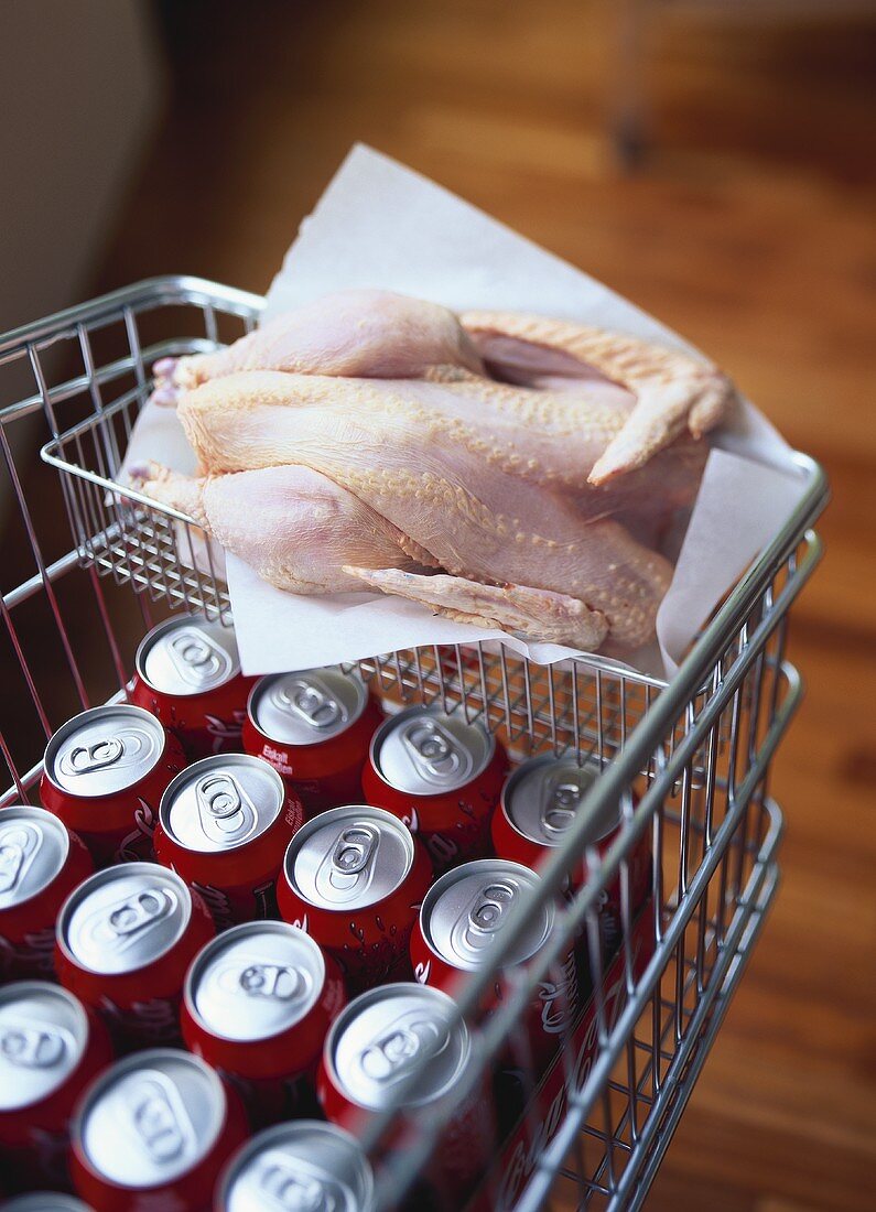 Cola tins in a shopping trolley with a raw chicken