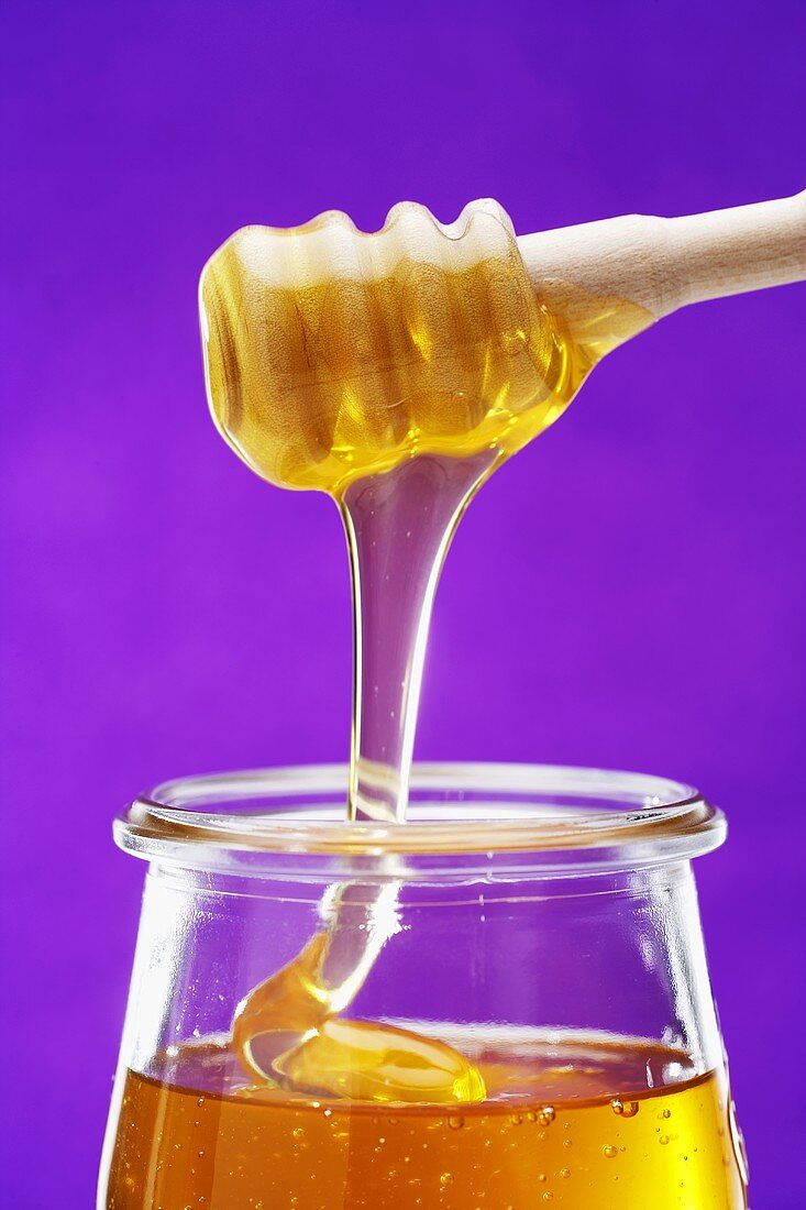 Honig fließt vom Honiglöffel in ein Glas