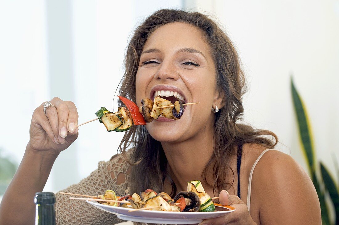 Young woman biting into grilled vegetable kebab