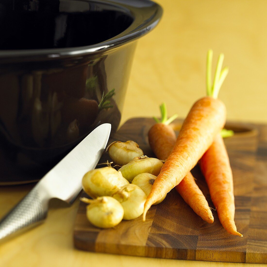 Zwiebeln und Karotten mit Messer auf einem Holzbrett