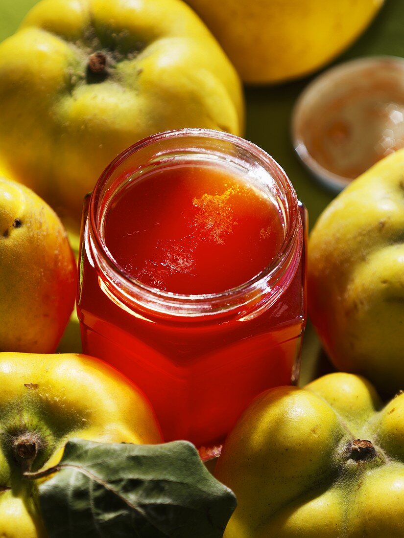 A jar of quince jelly surrounded by quinces