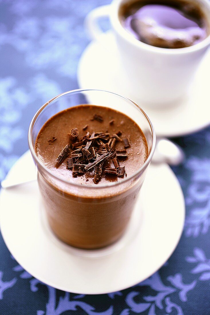 Mousse au chocolat im Glas, dahinter eine Tasse Kaffee