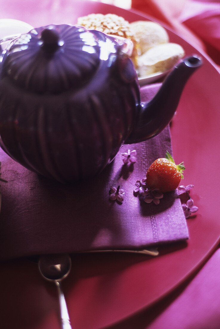 A teapot with small cakes in the background