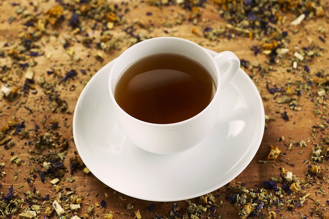 A cup of herb tea surrounded by dried herbs