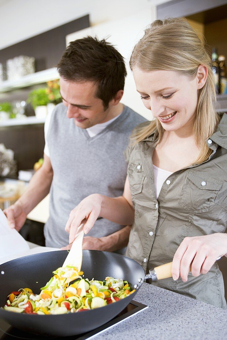 Man standing beside woman cooking vegetables in wok