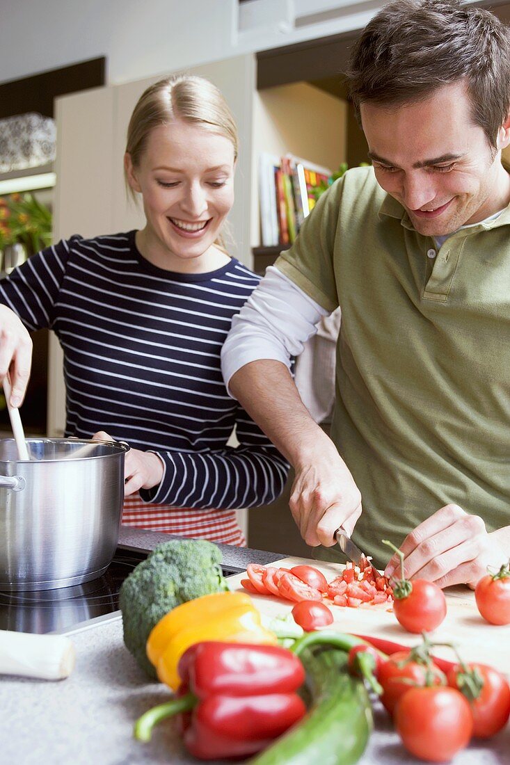 Mann schneidet Tomaten & Frau rührt im Kochtopf