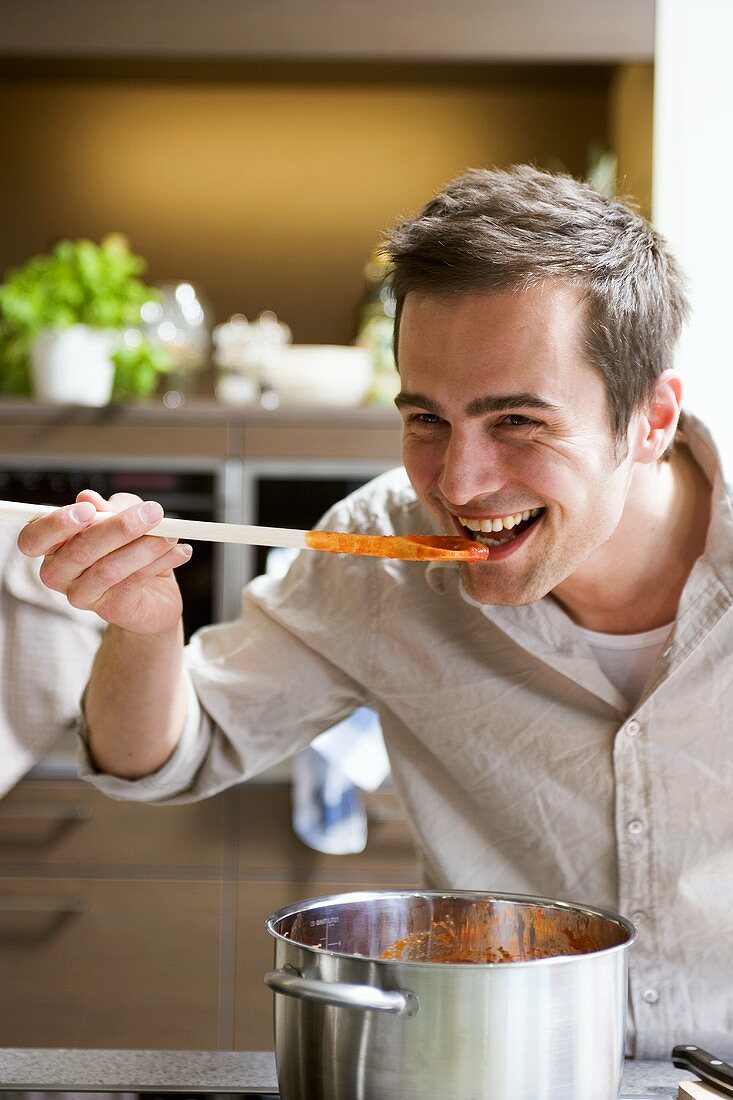 Young man tasting tomato sauce from wooden spoon