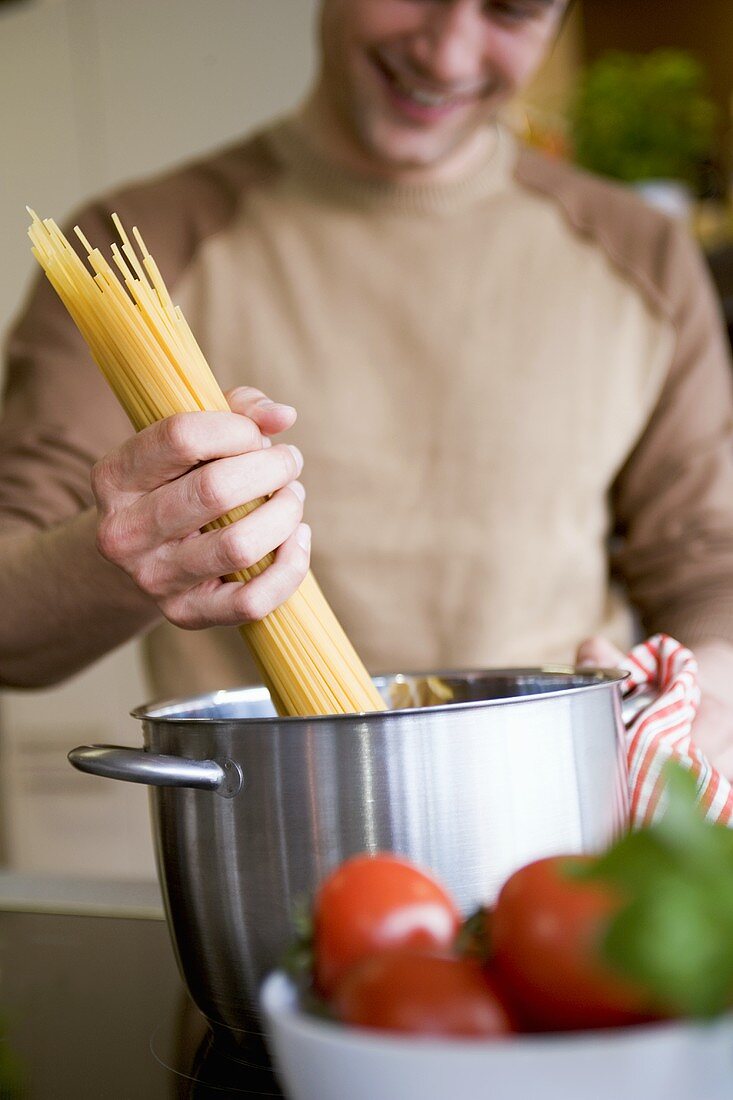 Junger Mann gibt Spaghetti in Topf