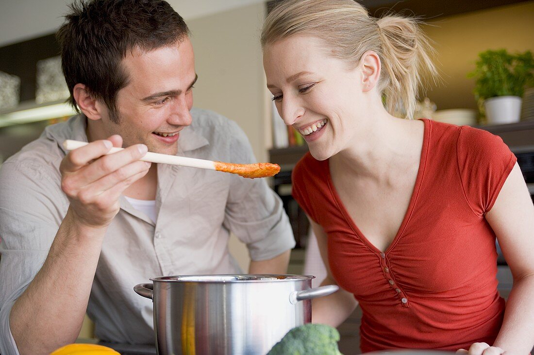 Young couple tasting tomato sauce from wooden spoon