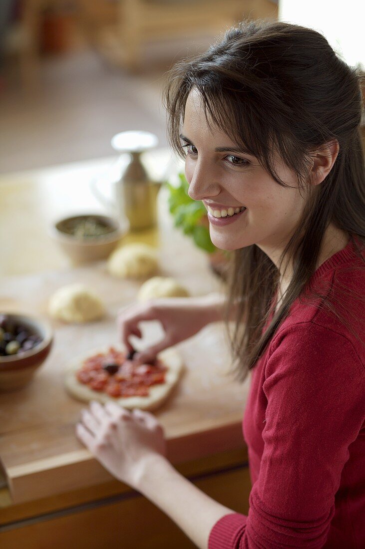Junge Frau belegt Mini-Pizza mit Oliven